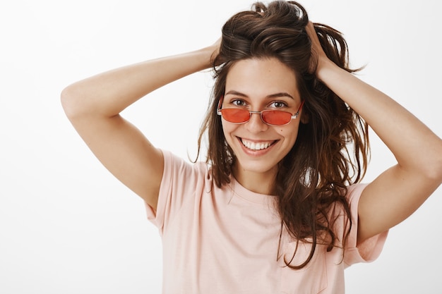 Stylish girl with sunglasses posing against the white wall