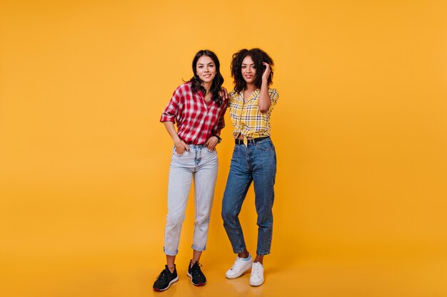 Stylish girlfriends in high spirits posing. Full-length shot of girls in trendy jeans.