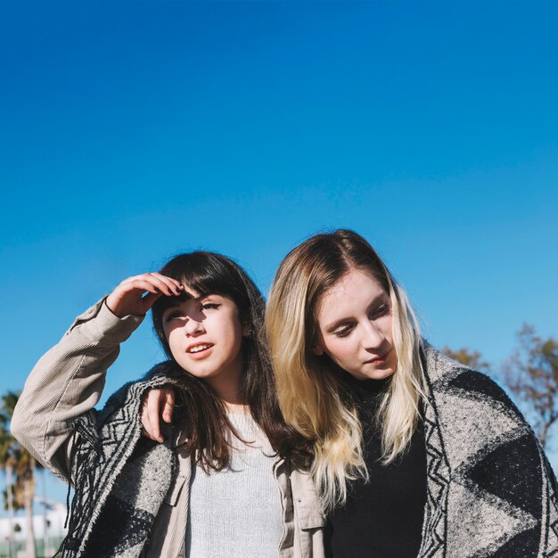 Stylish girls in scarf standing in embrace