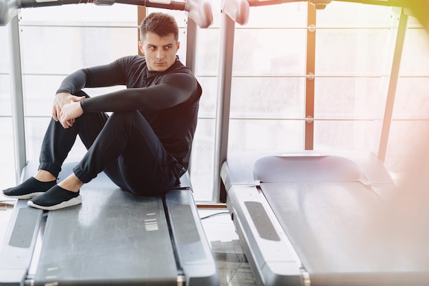 Stylish guy in the gym sits resting on the treadmill. Healthy Lifestyle.