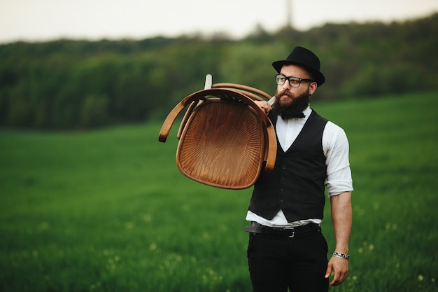 Free photo stylish guy holding a chair in the field