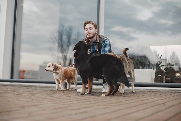 Stylish guy playing with a dogs. Man in autumn city.