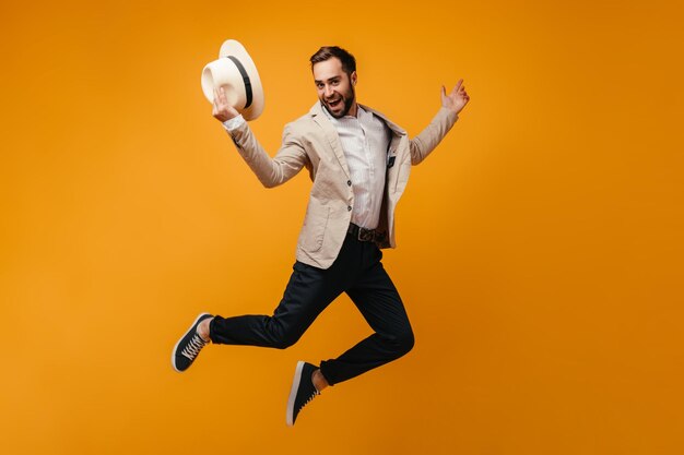 Stylish guy takes off hat and jumps high on isolated background