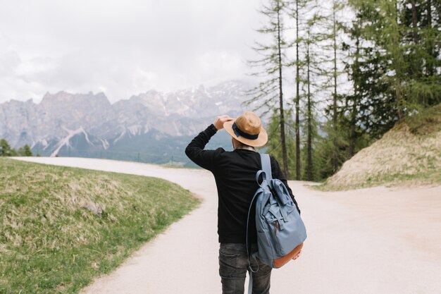 帽子をかぶったスタイリッシュな男は、春休みに外で過ごす山の風景を賞賛します