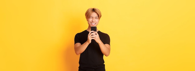 Stylish handsome asian guy taking picture on smartphone and smiling photographing with mobile phone