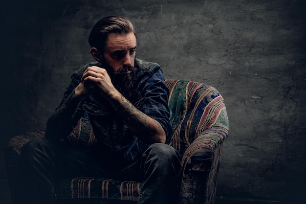 Stylish hipster male posing on a chair over grey background.