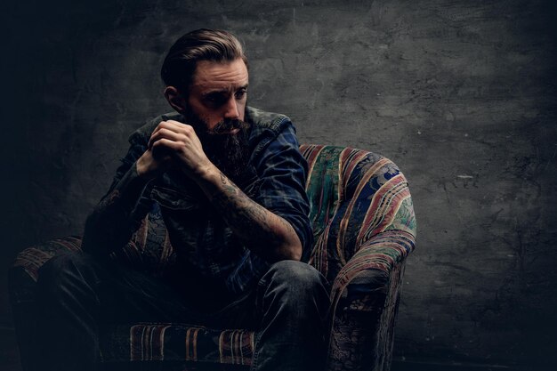 Stylish hipster male posing on a chair over grey background.