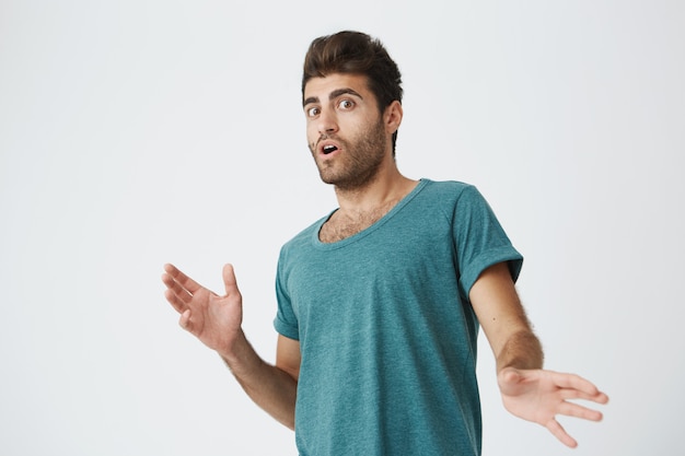 Free photo stylish hispanic young unshaven male with pop-eyed expression in blue tshirt being surprised news heard from friend. body language