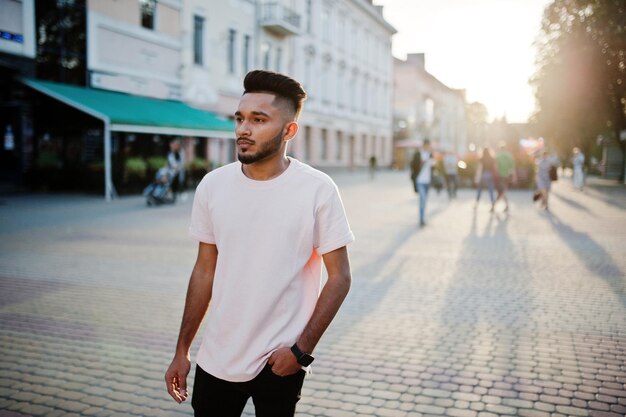 ピンクのTシャツでスタイリッシュなインドのひげの男インドのモデルは、街の夕日の通りで屋外でポーズをとった