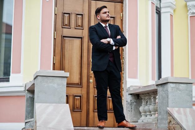 Elegante uomo d'affari indiano in abbigliamento formale in piedi contro la porta nel centro affari con le braccia incrociate