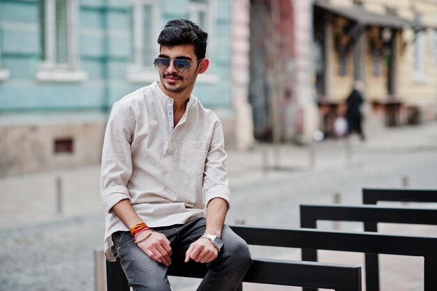캐주얼 옷과 선글라스를 쓴 세련된 인도 모델 남자가 인도 거리에서 야외 포즈를 취했습니다.