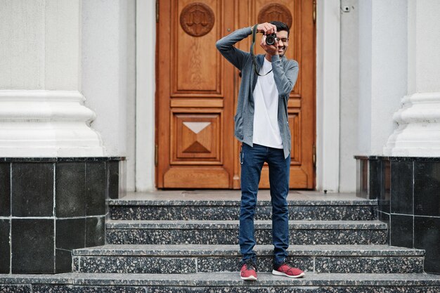 Stylish indian young man photographer wear casual posed outdoor with dslr photo camera at hands