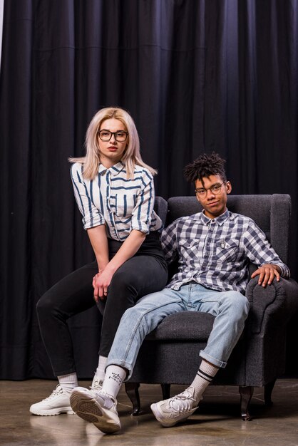 Stylish interracial young couple sitting on armchair looking at camera