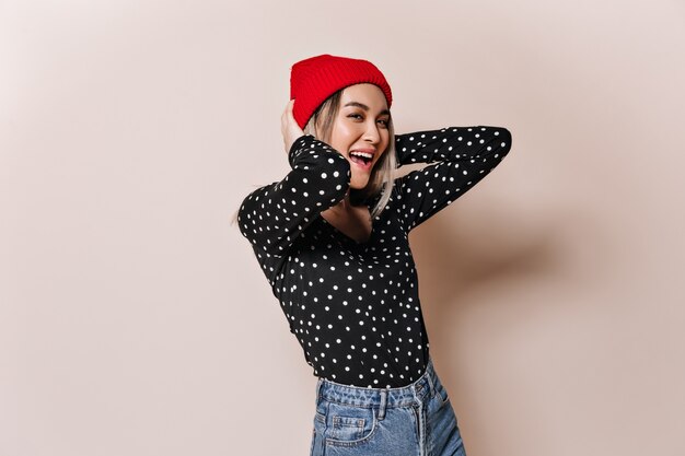 Stylish lady in red hat and plaid shirt has fun on beige wall