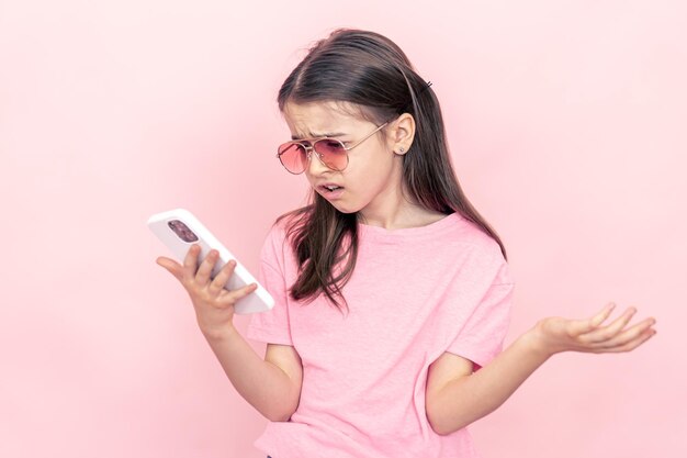 Free photo stylish little girl with a smartphone on a pink background