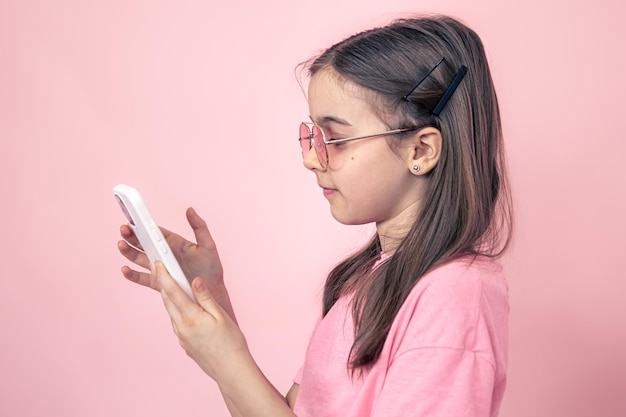 Bambina alla moda con uno smartphone su sfondo rosa