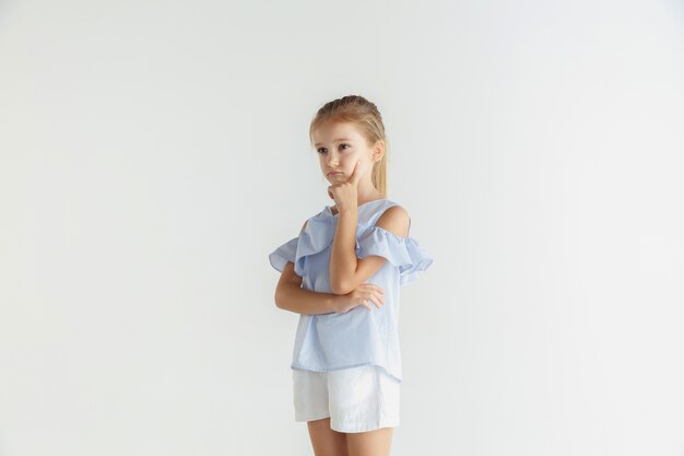 Stylish little smiling girl posing in casual clothes isolated. Caucasian blonde female model. Human emotions, facial expression, childhood. Thoughtful. Thinking, choosing.