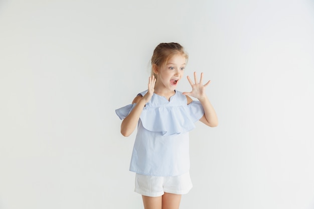 Elegante bambina sorridente in posa in abiti casual isolati sulla parete bianca. modello femminile biondo caucasico. emozioni umane, espressione facciale, infanzia, vendite. scioccato, stupito.