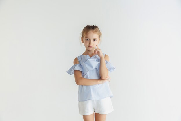 Stylish little smiling girl posing in casual clothes isolated on white wall. Caucasian blonde female model. Human emotions, facial expression, childhood. Thoughtful. Thinking, choosing.