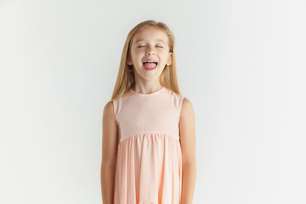 세련 된 작은 웃는 소녀 흰색 스튜디오 배경에 고립 된 드레스에 포즈. 백인 여성 모델. 인간의 감정, 표정, 어린 시절. 눈을 감고 웃음.