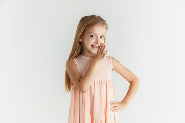 Стильная маленькая улыбающаяся девочка позирует в платье, изолированном на белой студии