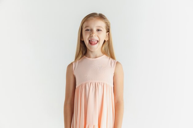 Stylish little smiling girl posing in dress isolated on white wall. Caucasian blonde female model. Human emotions, facial expression, childhood.