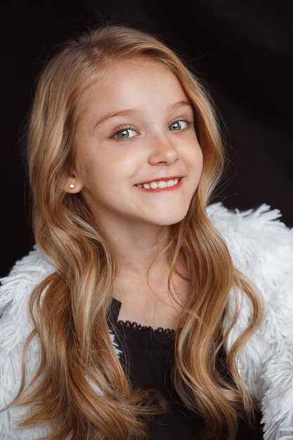 Stylish little smiling girl posing in white outfit isolated on black studio wall