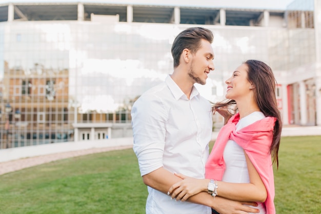 Stylish male office worker looking with love at brunette woman, standing with her on the street