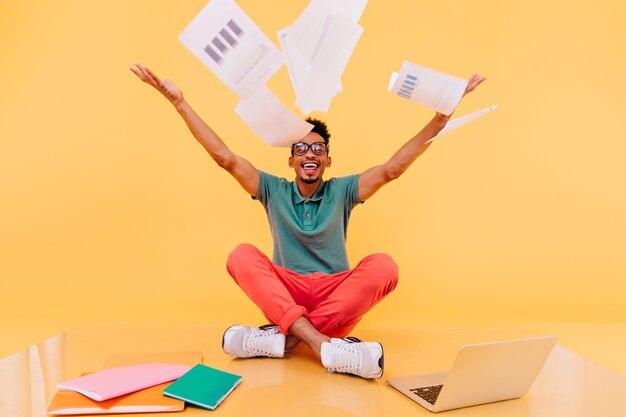 Stylish male student in white shoes fooling around. International freelancer in glasses having fun during work.