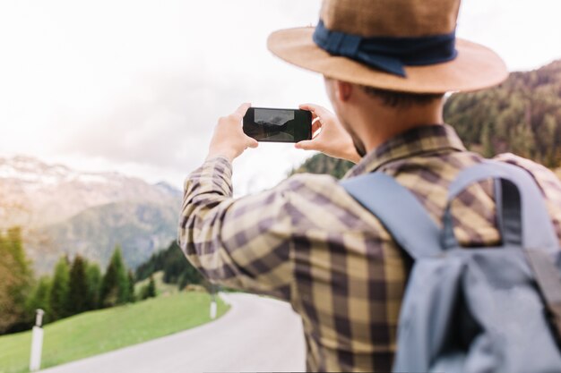 Stylish male traveler exploring Italy and taking picture of beautiful nature views holding his smartphone