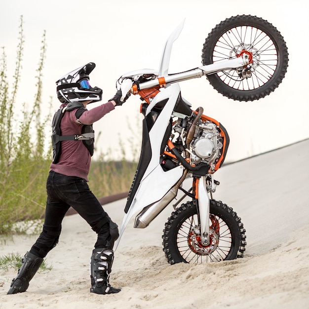 Stylish man raising motorbike in the desert