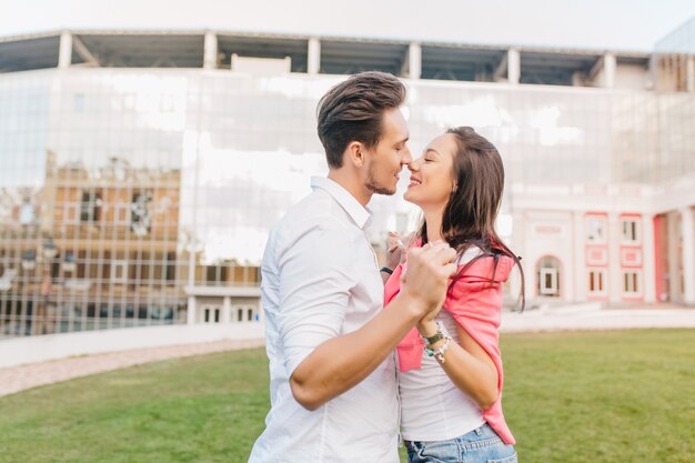 Stylish man with dark hair dancing with romantic woman on green lawn