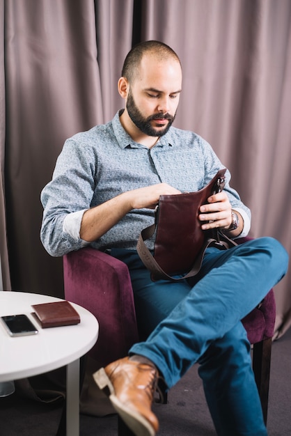 Foto gratuita uomo alla moda con borsa in poltrona