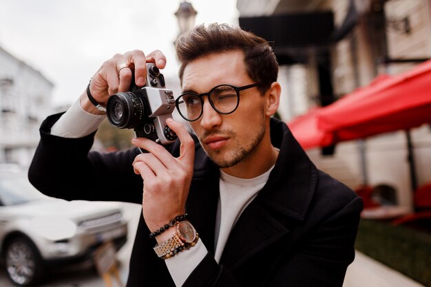 ヨーロッパの都市で写真を作る写真カメラを持つスタイリッシュな男。