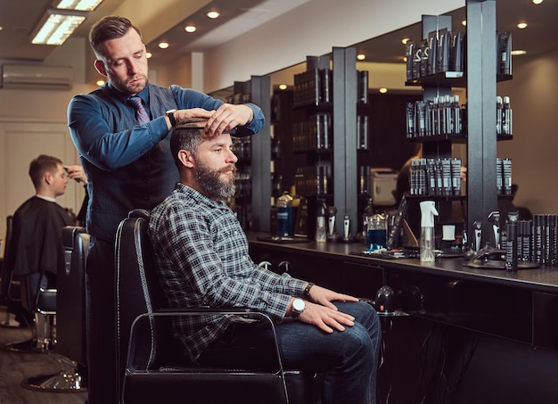 A stylish Master barber does a haircut to the client. Men's haircut in a barbershop. Styling hair with a comb.