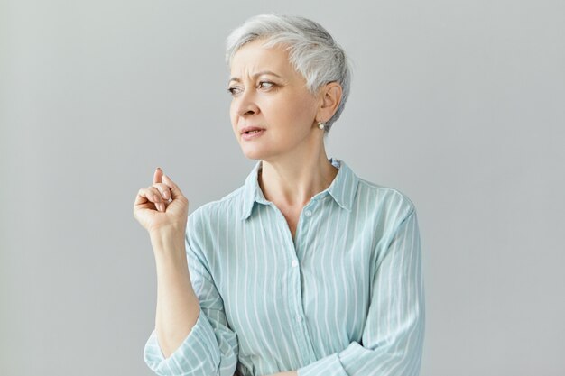 Stylish mature woman professor or couch with pixie haircut looking away, raising fore finger, saying something, giving lecture, sharing her life experience.