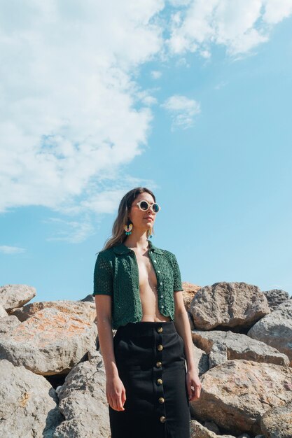 Stylish model in green jacket with eyeglasses standing against stacked rocks