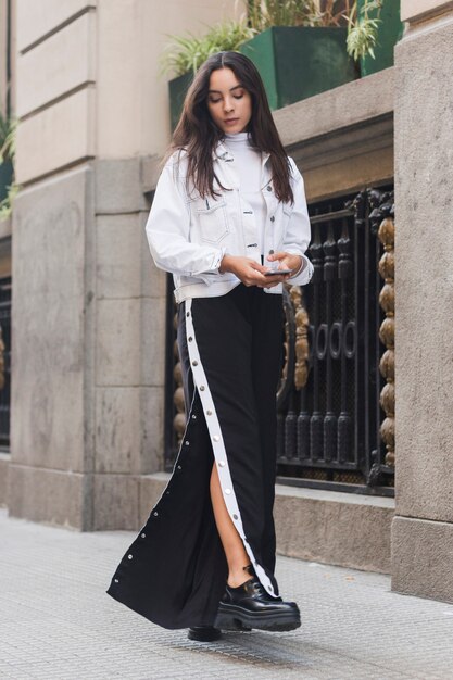 Stylish modern young woman walking on sidewalk in city