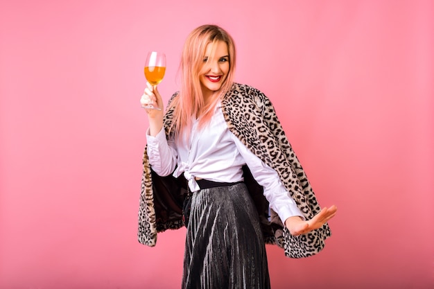 Стильная позитивная симпатичная молодая женщина веселится, одетая в вечерний сверкающий коктейльный наряд и модное пальто с меховым леопардовым принтом, розовый фон, наслаждаясь вечеринкой зимних праздников.