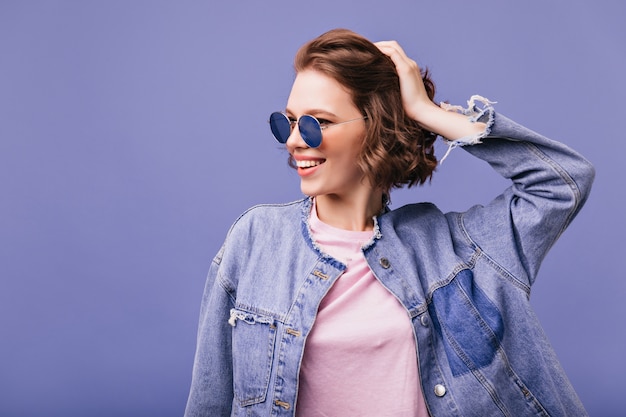 Stylish pretty girl in sunglasses touching her short wavy hair with smile. wonderful caucasian woman laughing.