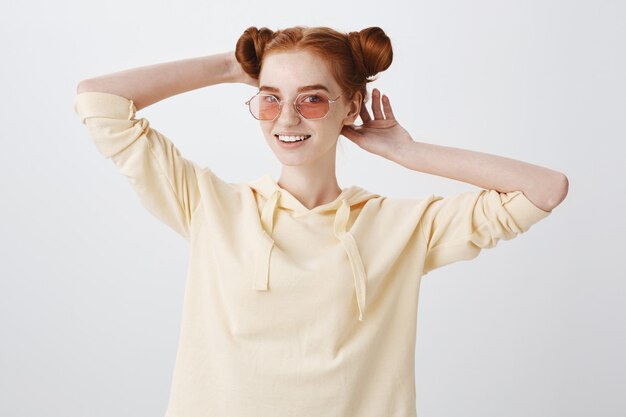 Stylish redhead teenage girl in sunglasses fixing haircut