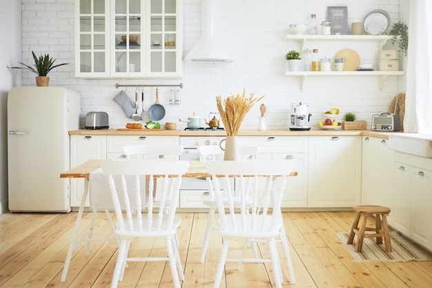 Stylish Scandinavian kitchen interior: chairs and table in foreground, fridge, long wooden counter with machines, utensils on shelves. Interiors, design, ideas, home and coziness concept