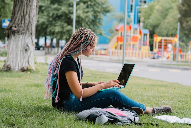 Scolara alla moda nel parco con il computer portatile