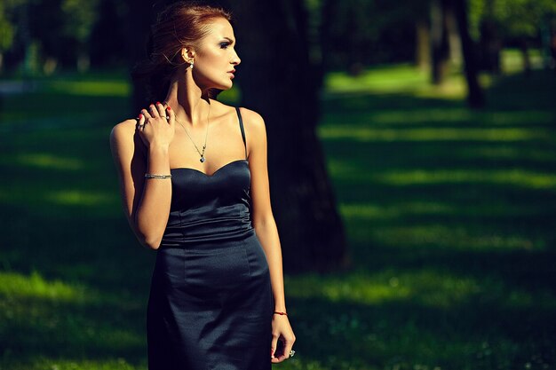 공원에서 포즈 검은 드레스에 세련 된 섹시 한 아름 다운 젊은 여자 모델