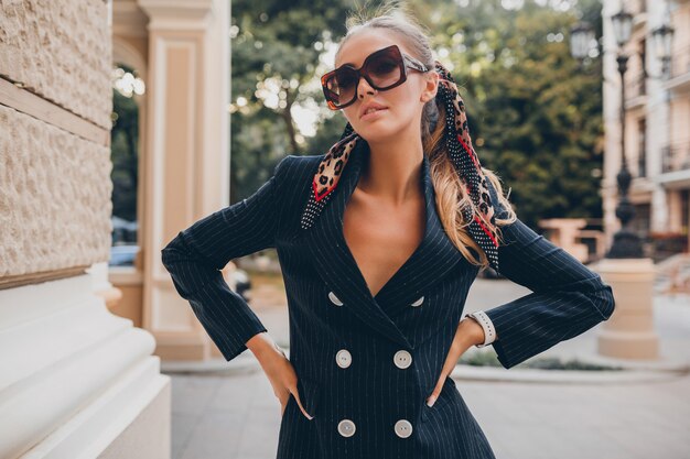 Stylish sexy woman dressed in elegant tuxedo suit walking in city on summer spring day