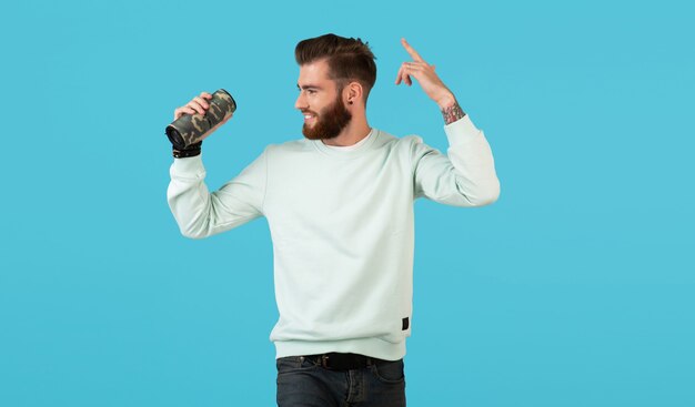 Stylish smiling young man holding wireless speaker listening to music on blue