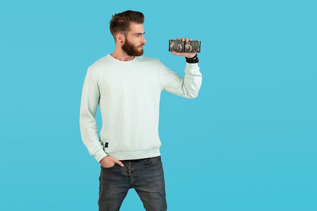 Stylish smiling young man holding wireless speaker listening to music on blue