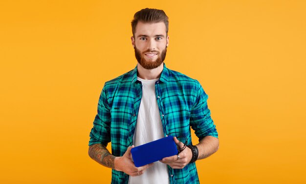 Stylish smiling young man holding wireless speaker listening to music colorful style happy mood isolated on yellow background