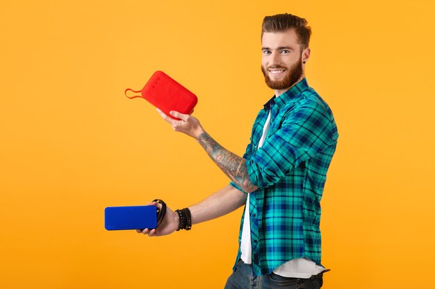 Stylish smiling young man holding wireless speaker listening to music