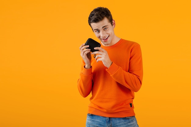 Stylish smiling young man in orange sweater holding wireless speaker happy listening to music 